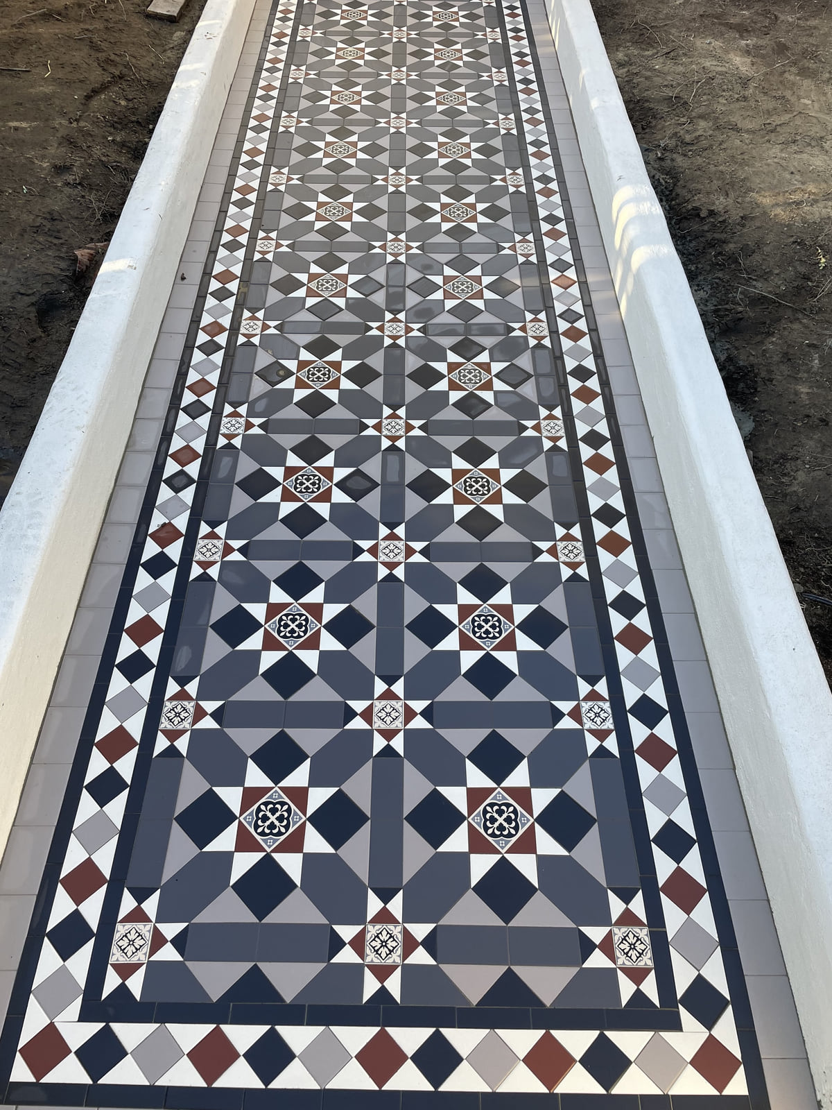 Top-down view of a Fitzroy path in grey, blue, red and black between marble kerbs, Drummoyne